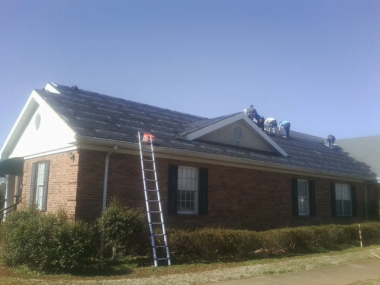 Crew tearing shingles off a brick ranch roof with a ladder set — Emergency Roof Repair work by our crew in Veneta