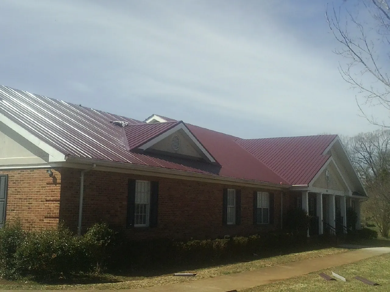 Red metal roof with gabled entries on a long brick building, from a Hail Damage Roof Repair job in Veneta