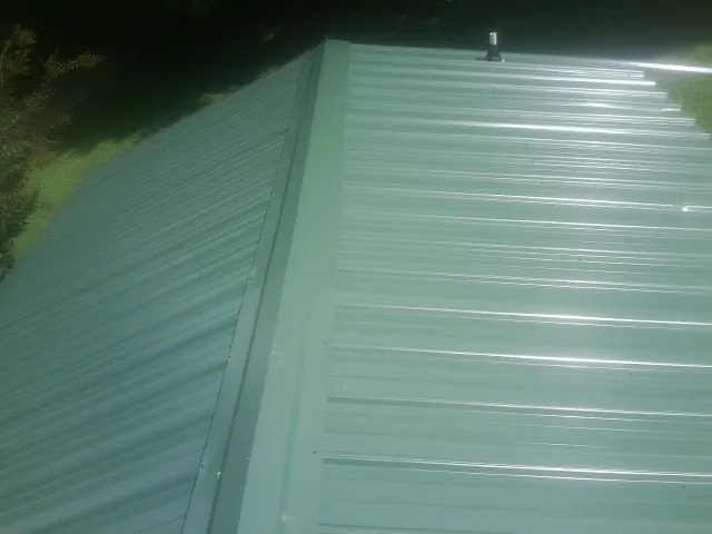 New green metal panels meeting at the ridge of a roof — Flat Roof Repair work by our crew in Veneta