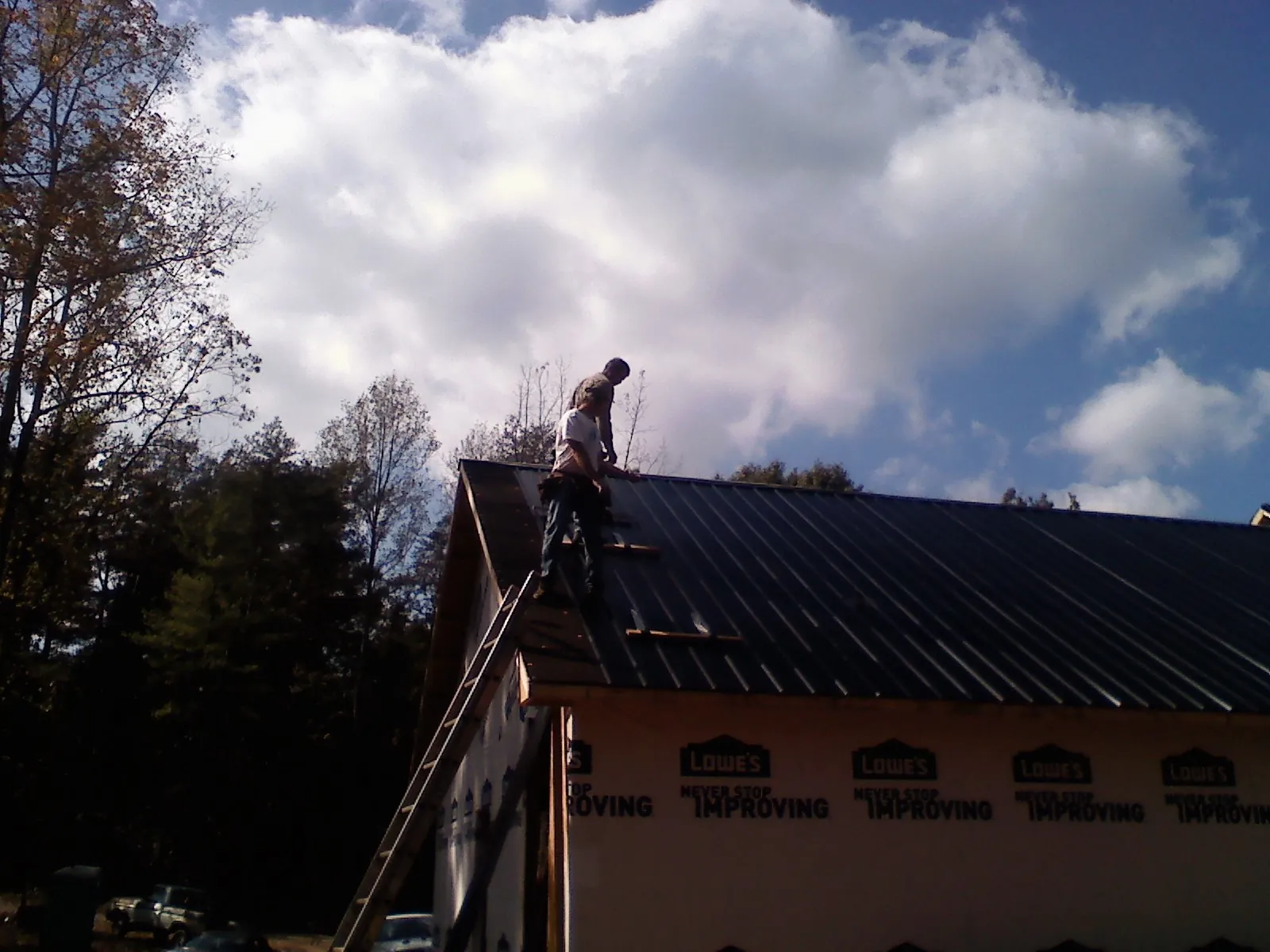 Roofer fastening dark metal panels high against a cloudy sky, from a Roof Inspection job in Veneta