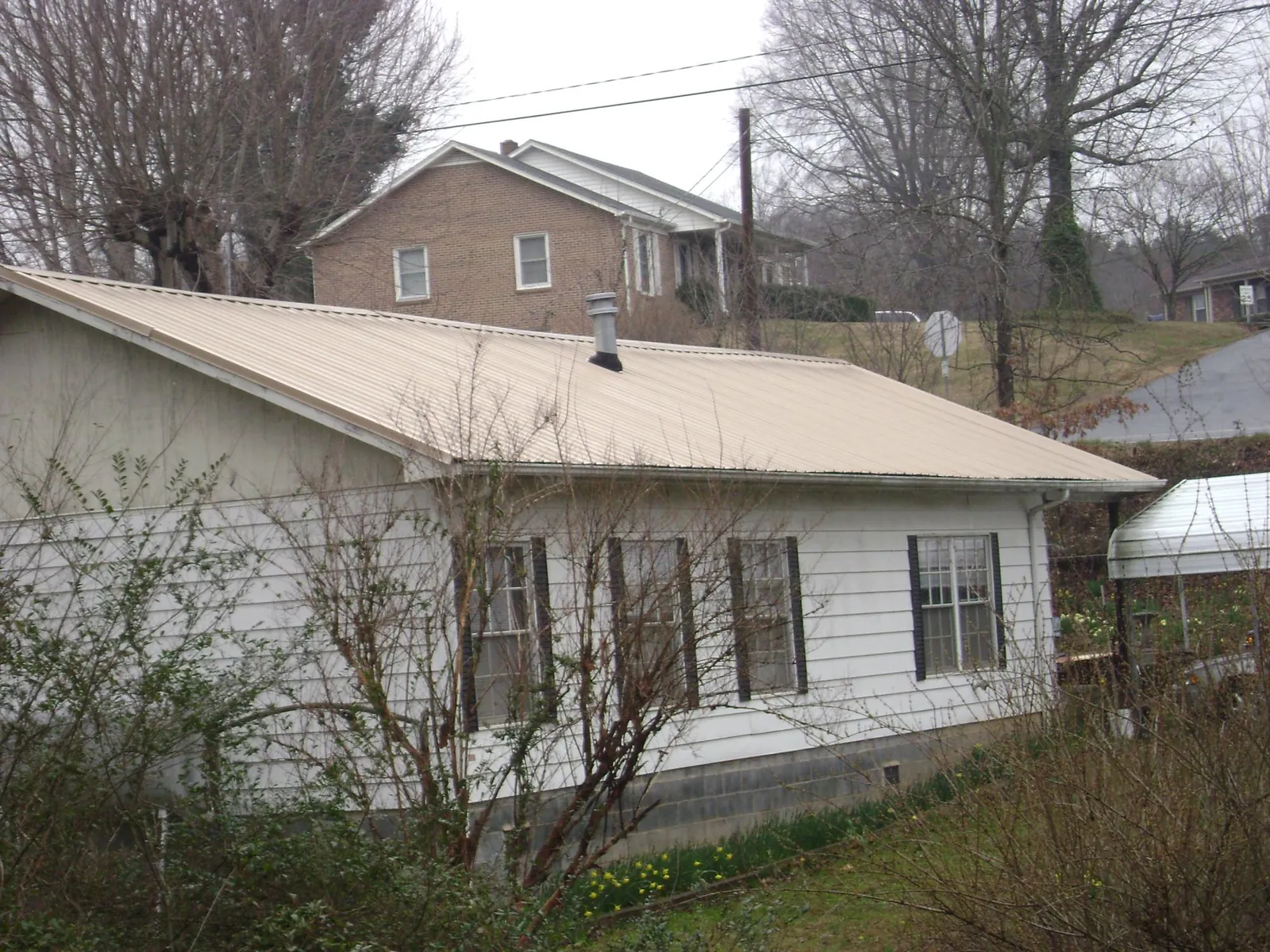 Tan metal roof on a white sided house set into a hillside — Commercial Roofing by Roofing Brothers in Veneta